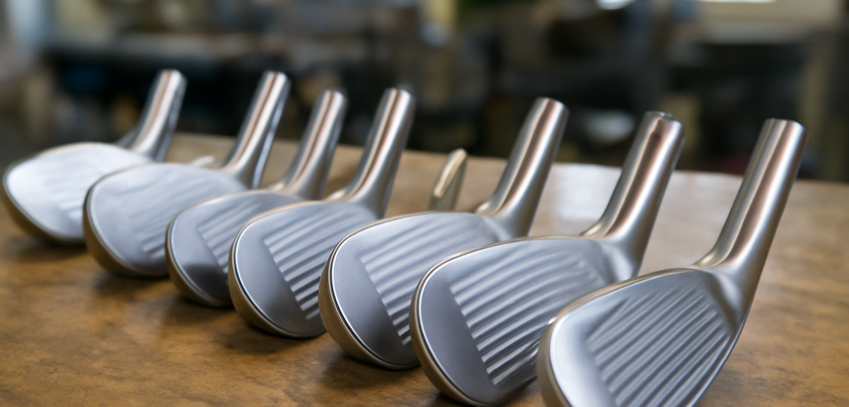 Golf club heads arranged on a workbench in a manufacturing workshop, photorealistic, no text