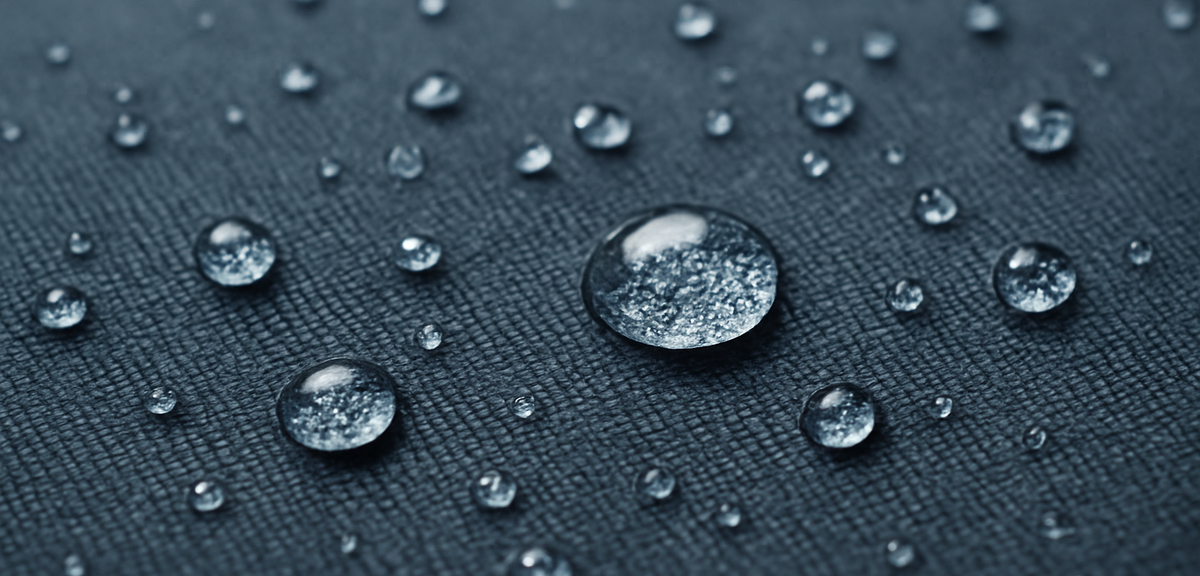 Close-up of water droplets beading on a water-repellent fabric surface, photorealistic, no text
